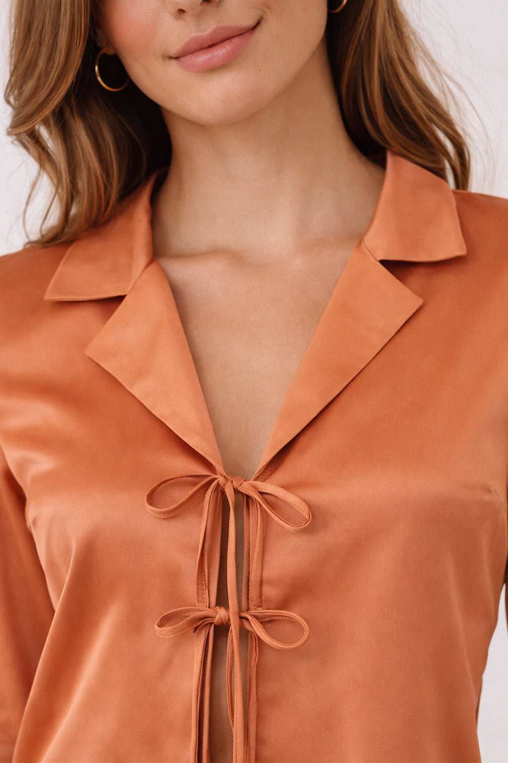 Close-up of a person wearing an orange blouse with a bow detail.