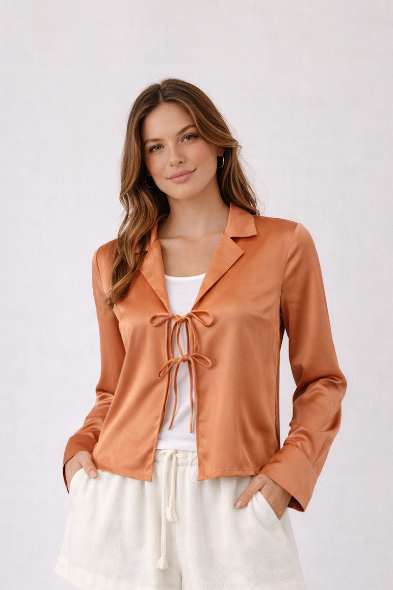 Woman wearing a brown satin jacket over a white top on a plain background