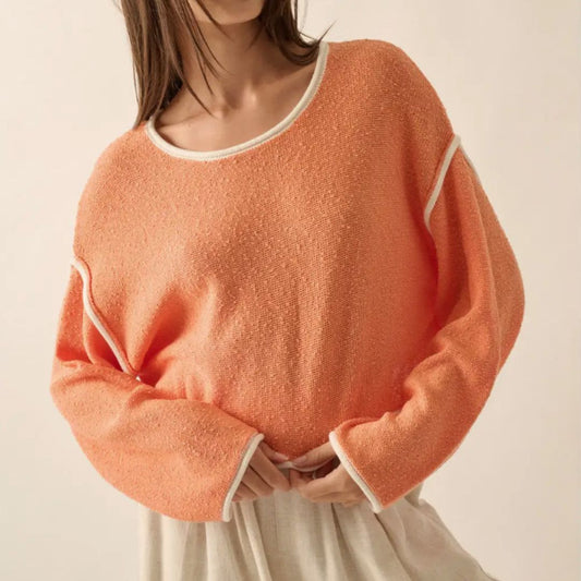 A person wearing an orange, cropped-style, knit sweater with exposed seams.