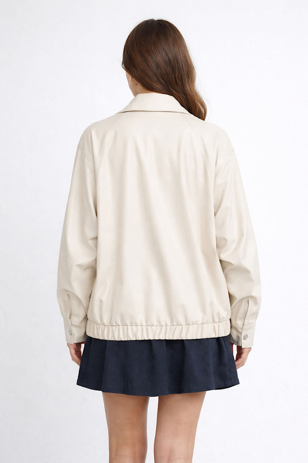 Person wearing a beige jacket and navy skirt on a white background