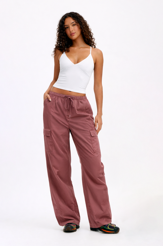 Woman wearing a white tank top and pink cargo pants on a white background