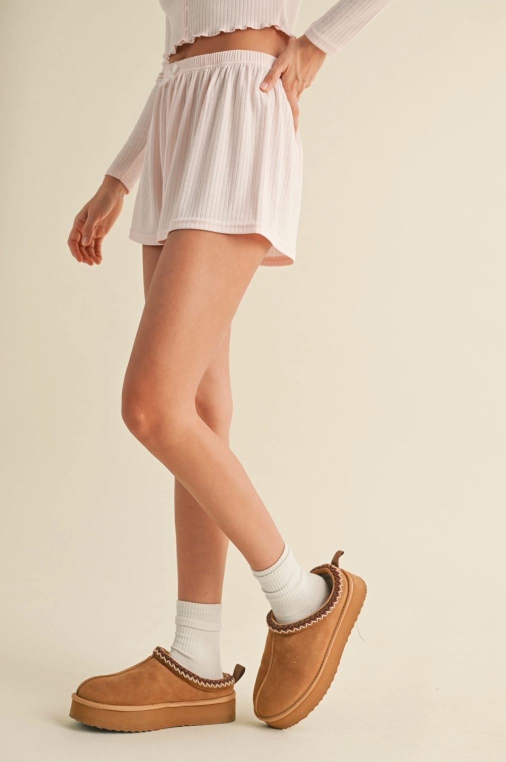 Person wearing a white skirt, white top, and brown shoes on a beige background