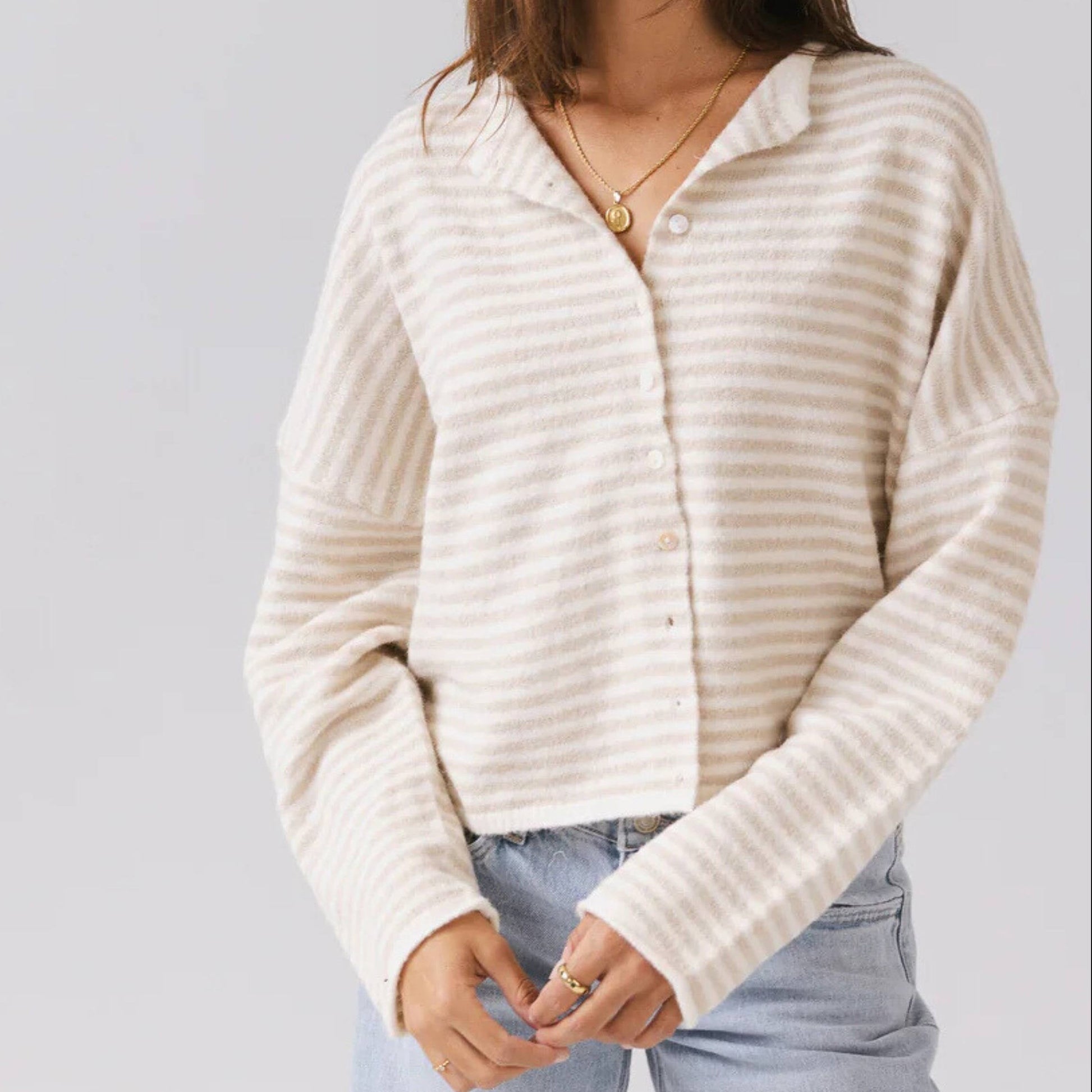 Woman wearing a cream ribbed sweater and light blue jeans against a plain background