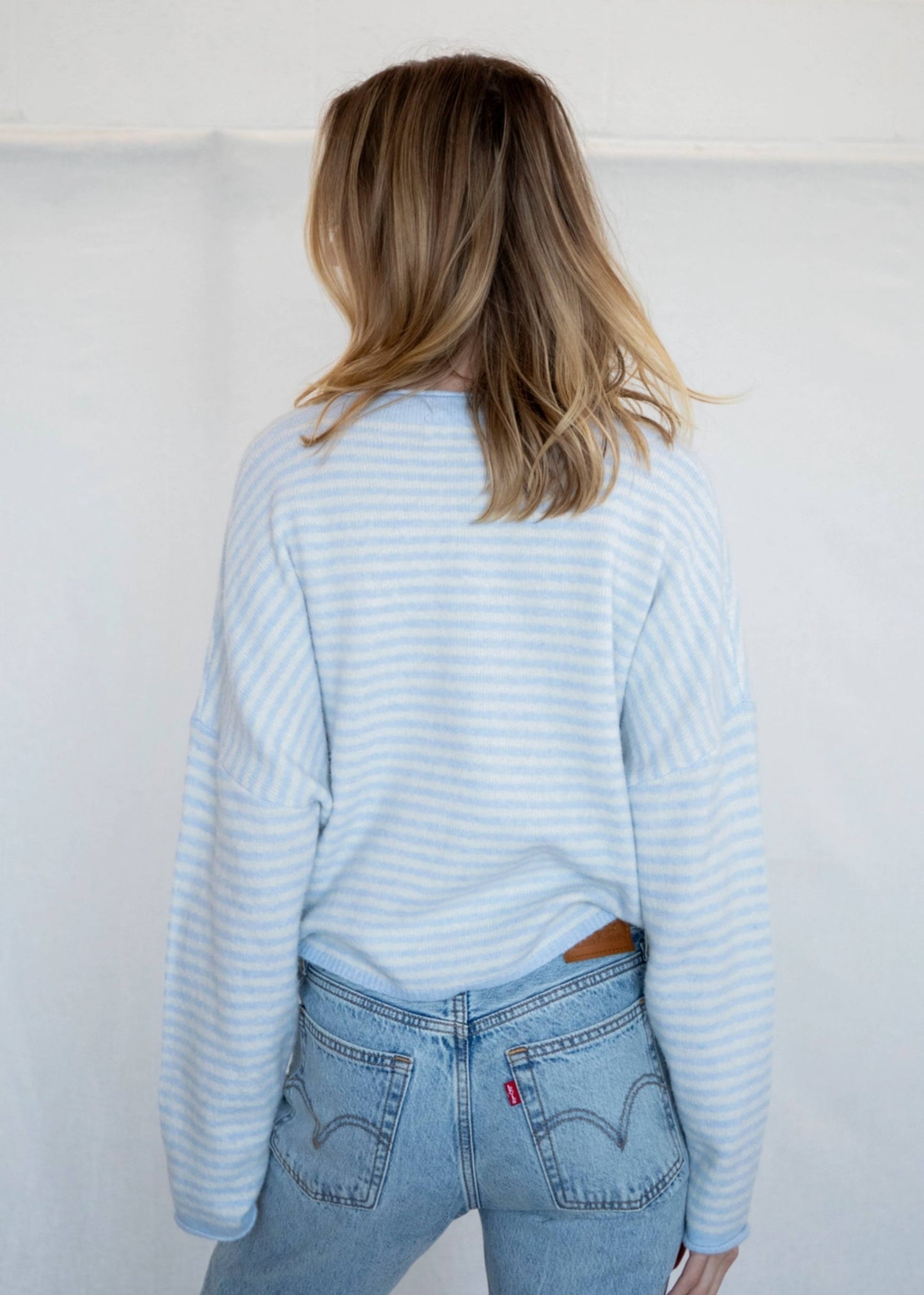 Person wearing a light blue striped sweater and jeans against a white background