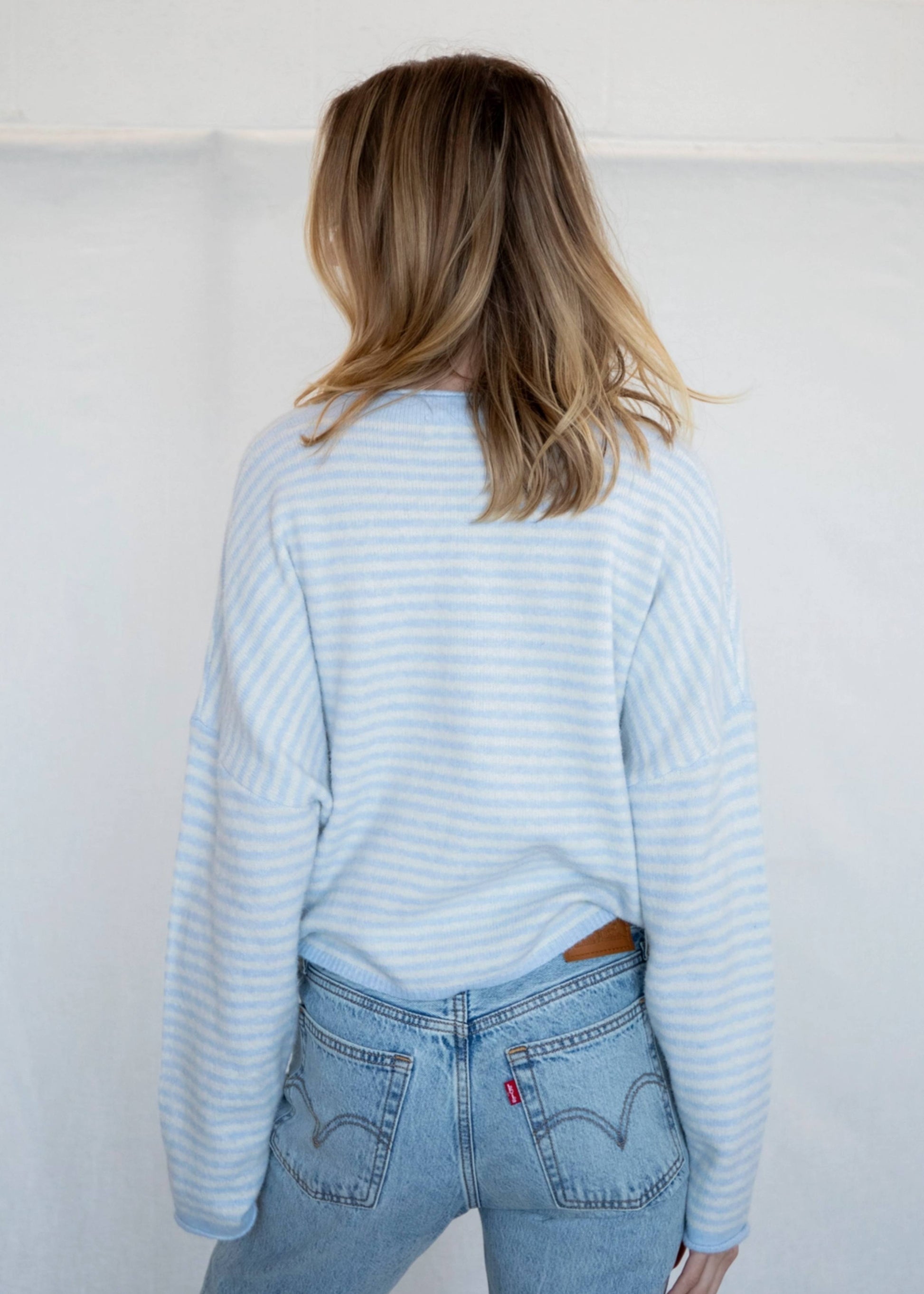 Person wearing a light blue striped sweater and jeans against a white background