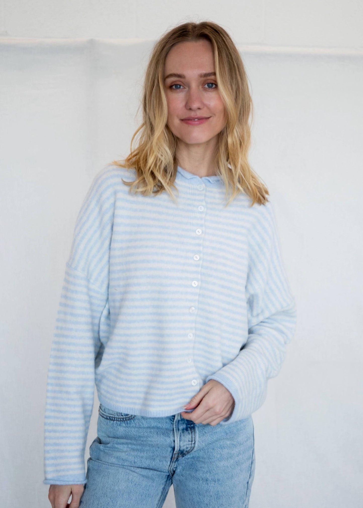 Woman wearing a light blue striped sweater and jeans against a white background