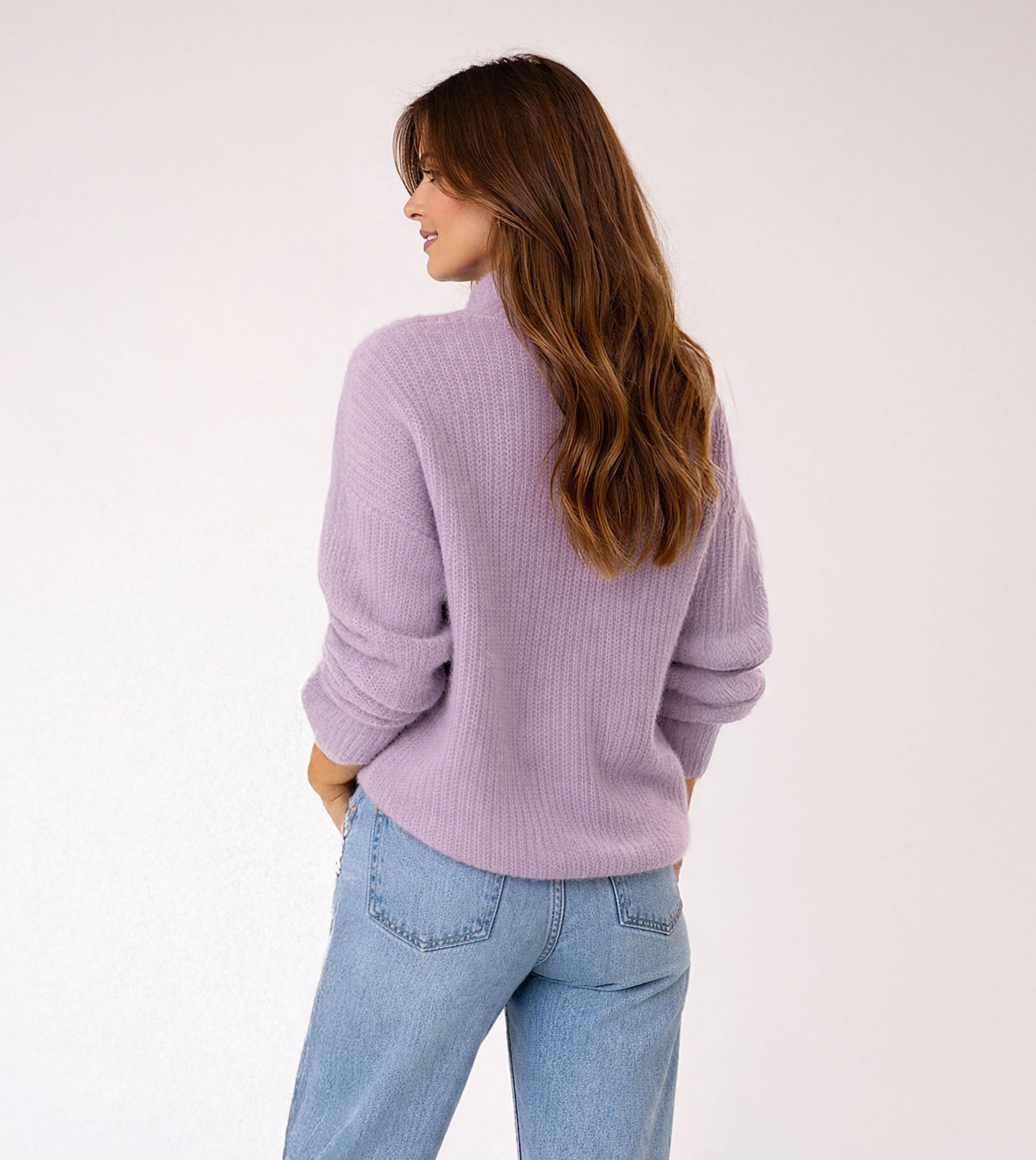 Woman wearing a light purple sweater and blue jeans on a white background