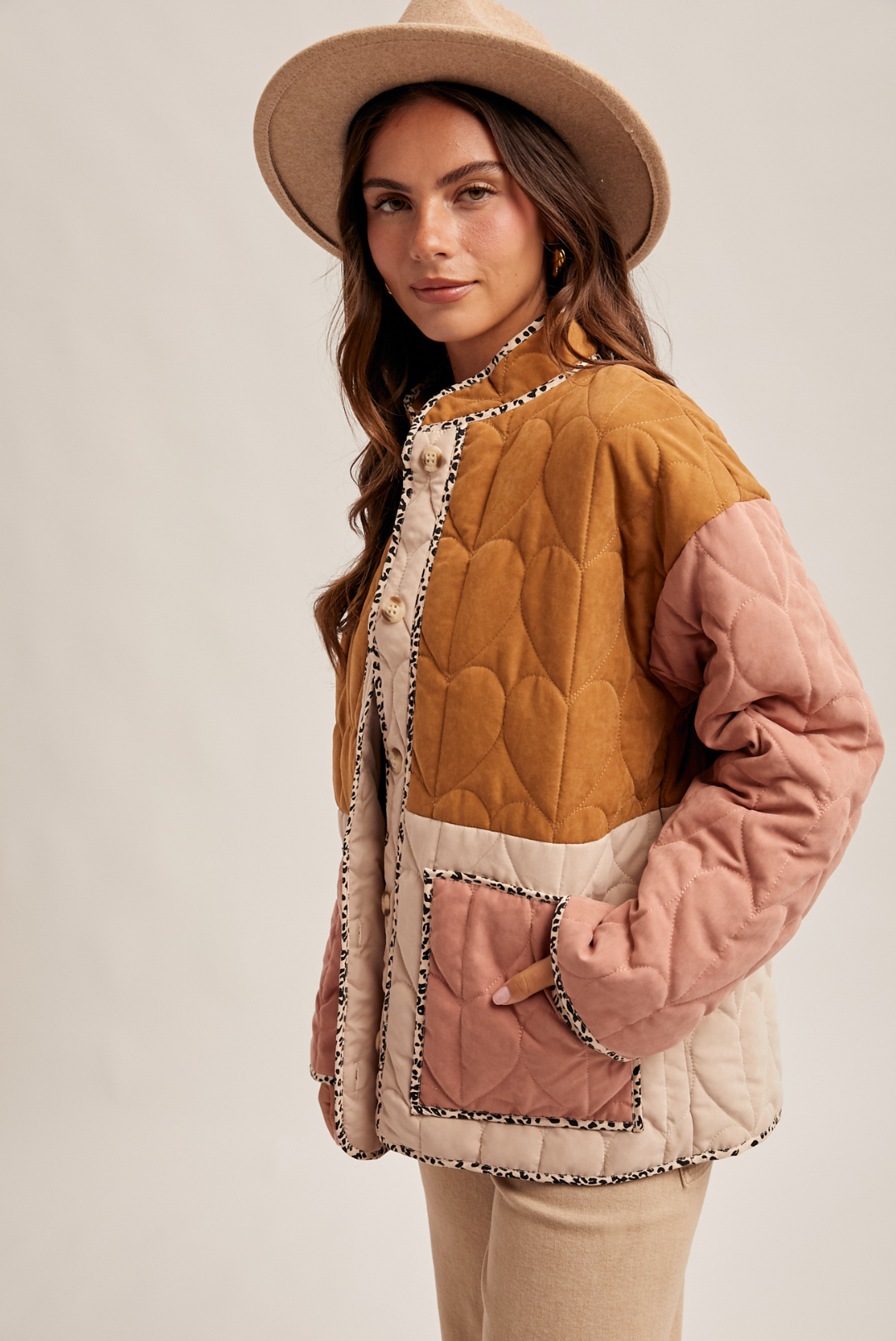 Woman wearing a quilted jacket with a beige hat on a plain background