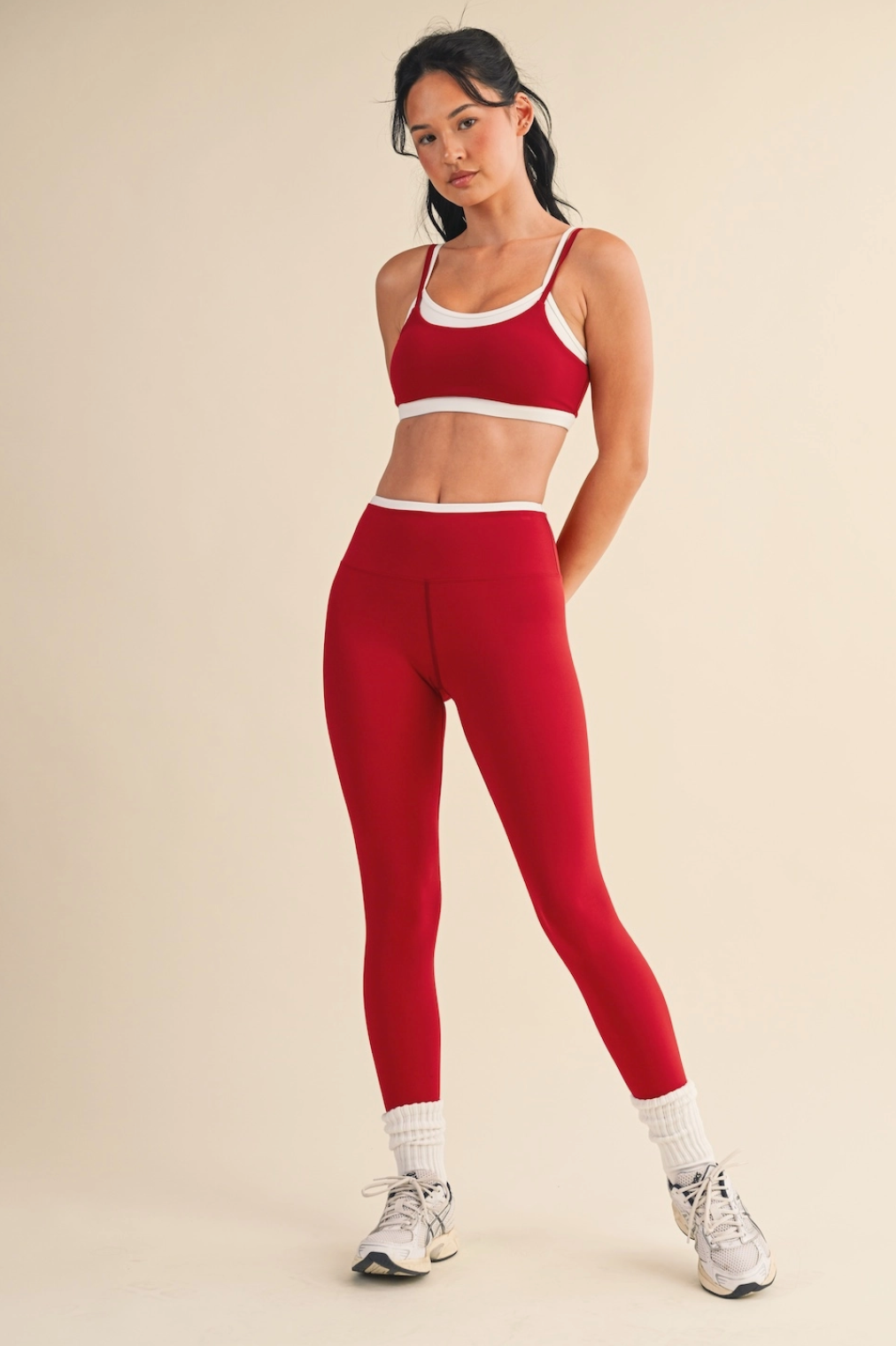 Woman wearing a red sports bra and leggings set on a beige background