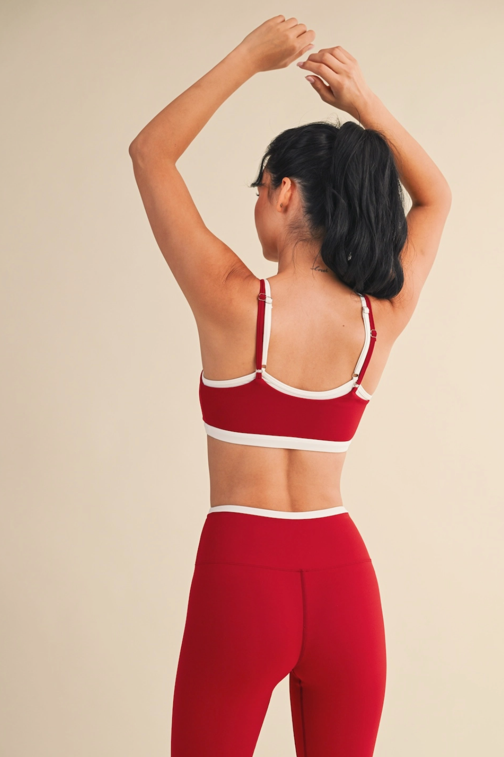Person wearing a red sports bra and leggings on a beige background