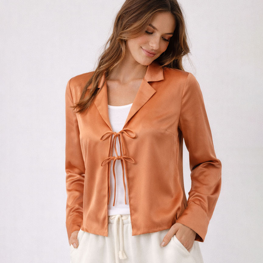 Woman wearing a rust-colored satin jacket with a white top and pants on a light background