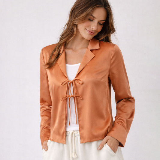 Woman wearing a rust-colored satin jacket with a white top and pants on a light background