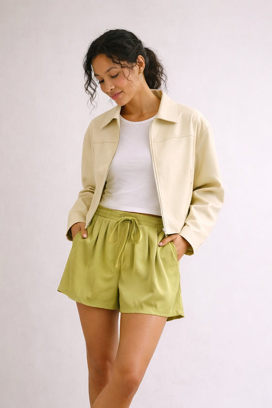 Woman wearing a light jacket, white shirt, and green shorts on a plain background
