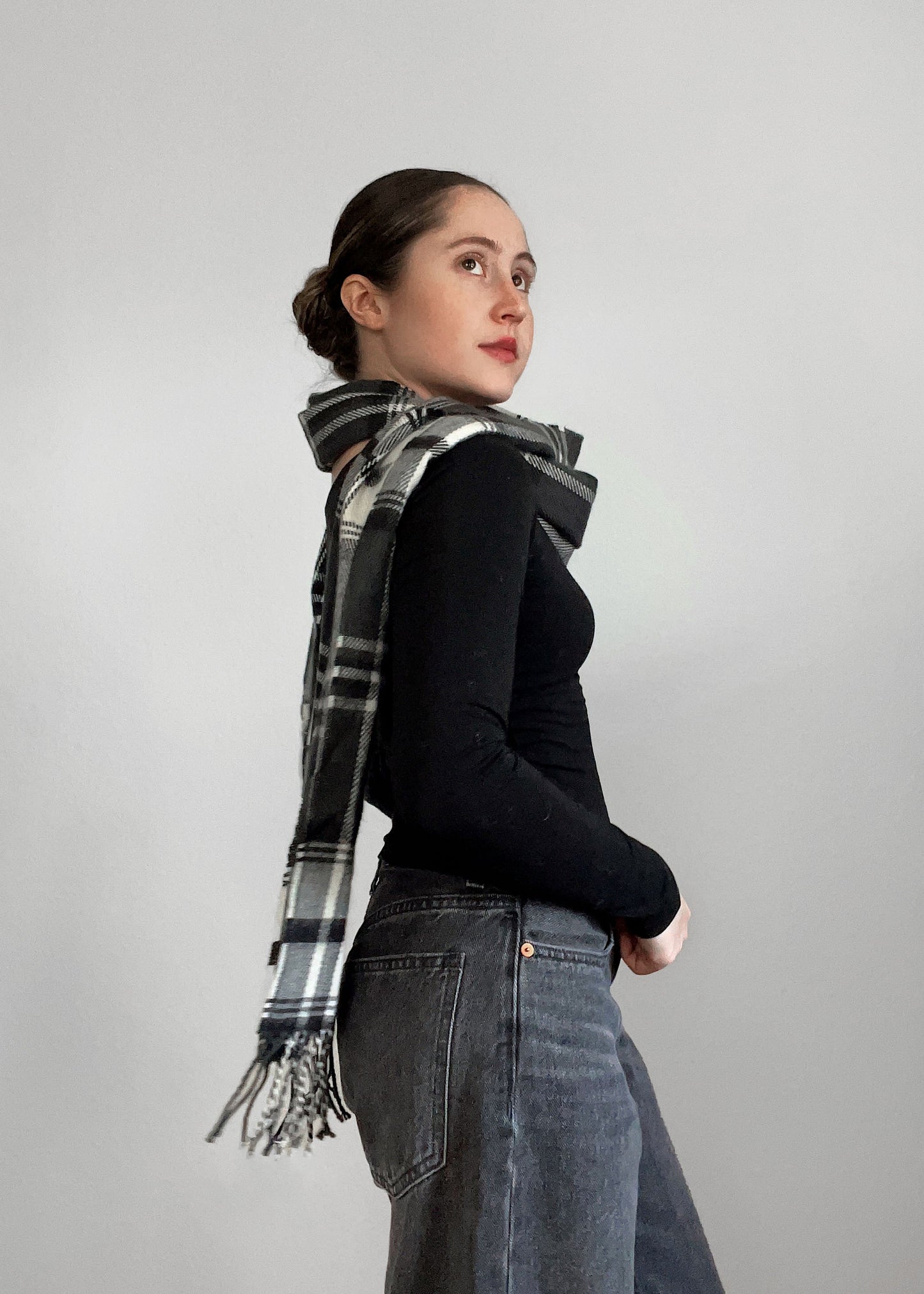 Woman wearing a black sweater and plaid scarf against a gray background