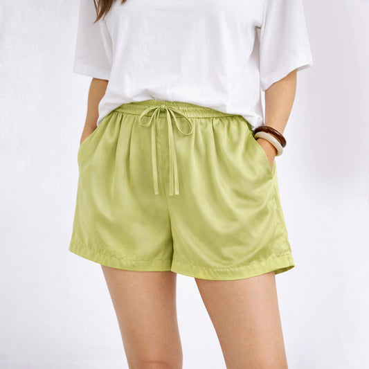 Person wearing light green shorts and a white top on a plain background