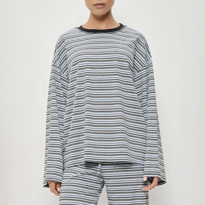 A model wearing a matching long-sleeve striped lounge set, featuring a loose crewneck top and coordinating pants in a gray, black, and white horizontal stripe pattern.