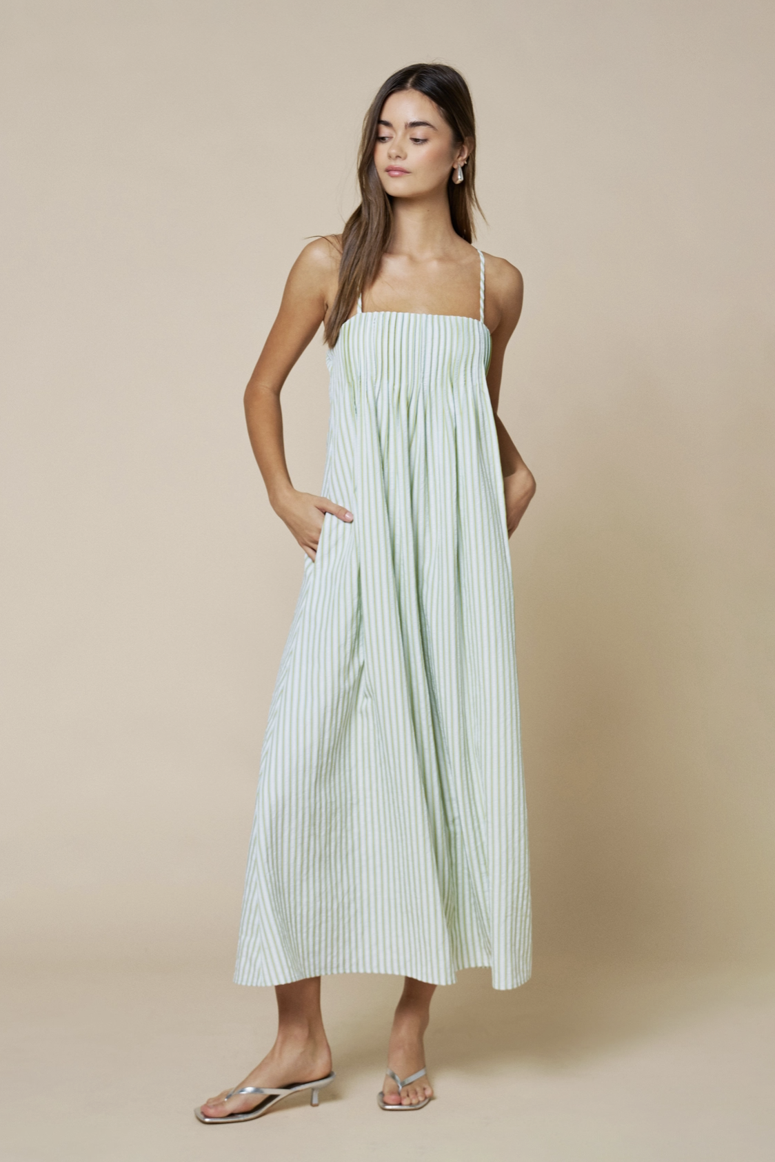 Woman wearing a light green striped dress against a beige background