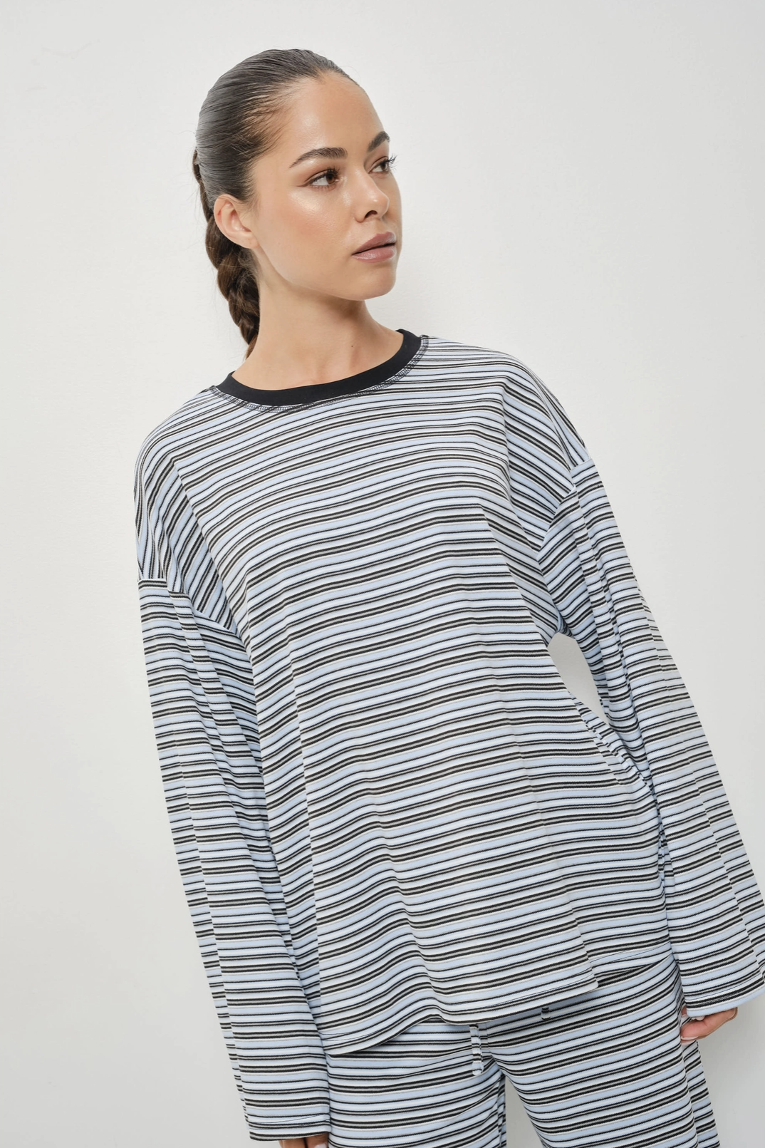 A woman wearing a long-sleeve striped top and matching pants in a gray, white, and black horizontal stripe pattern, photographed against a plain light gray studio background.