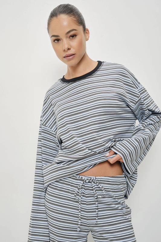 A woman modeling a matching two-piece loungewear set featuring a long-sleeve cropped top and drawstring pants, both in a gray and white striped pattern with a black crew neck trim.