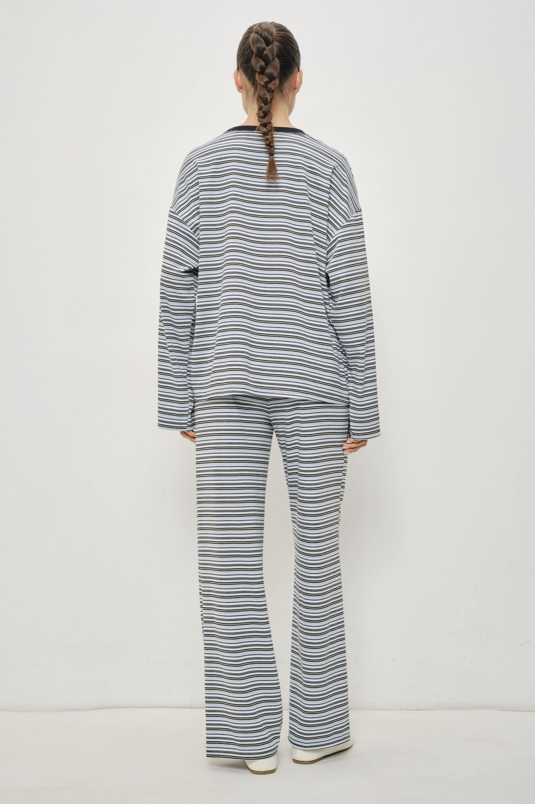 A model viewed from behind wearing a matching two-piece lounge set with thin horizontal navy and gray stripes on a white background.