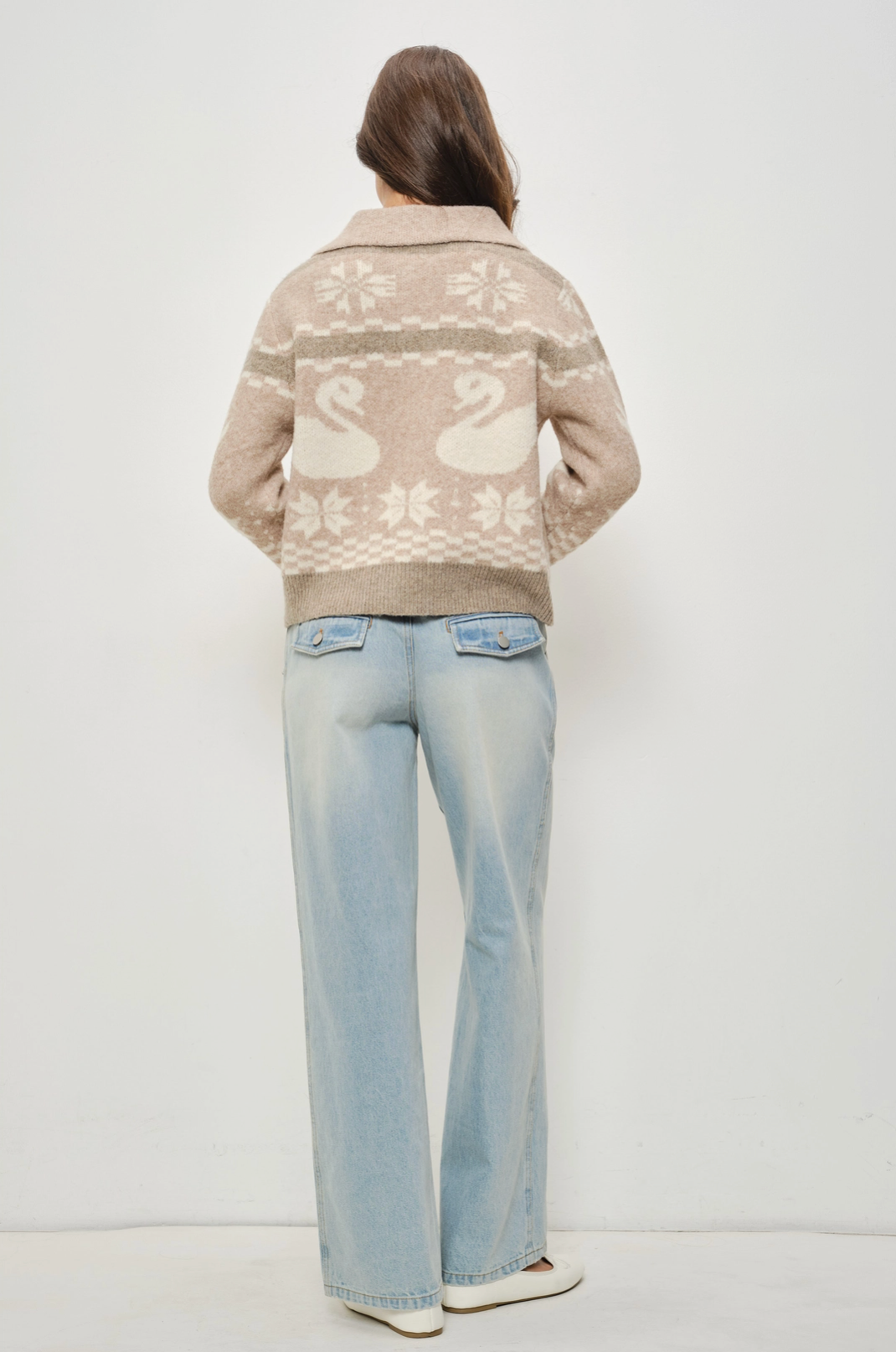 Person wearing a patterned sweater and light blue jeans on a white background