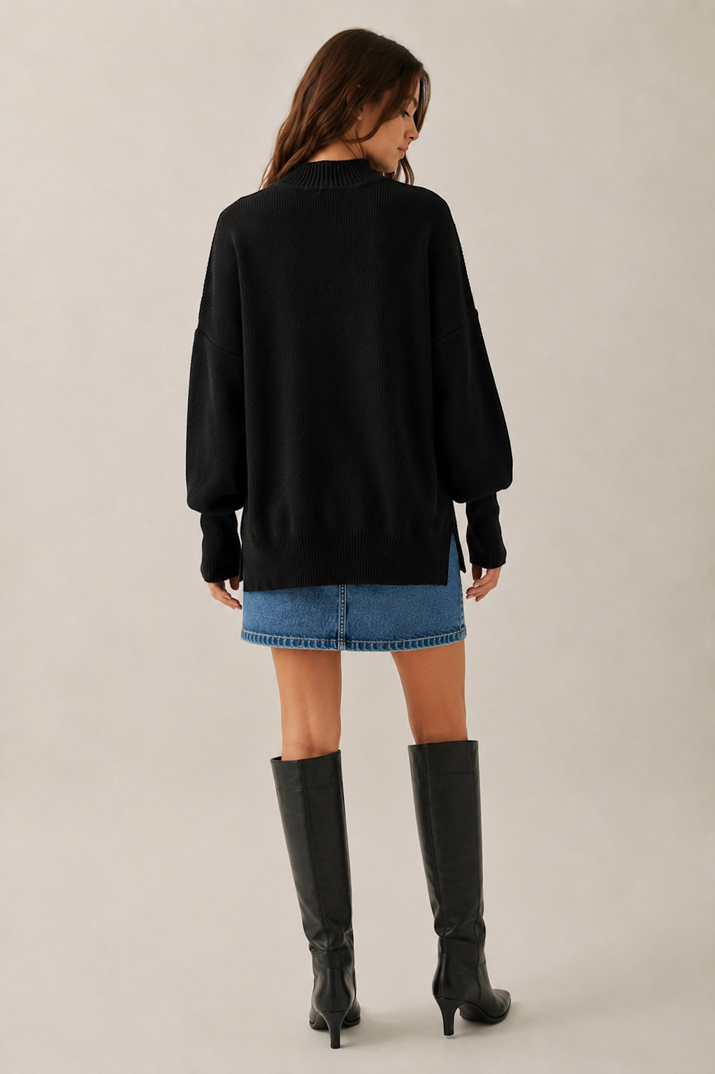 Person wearing a black sweater, denim shorts, and black knee-high boots on a plain background