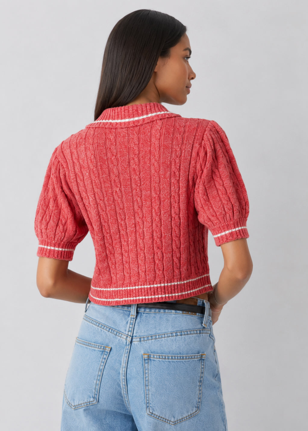 Person wearing a red textured top and blue jeans on a gray background