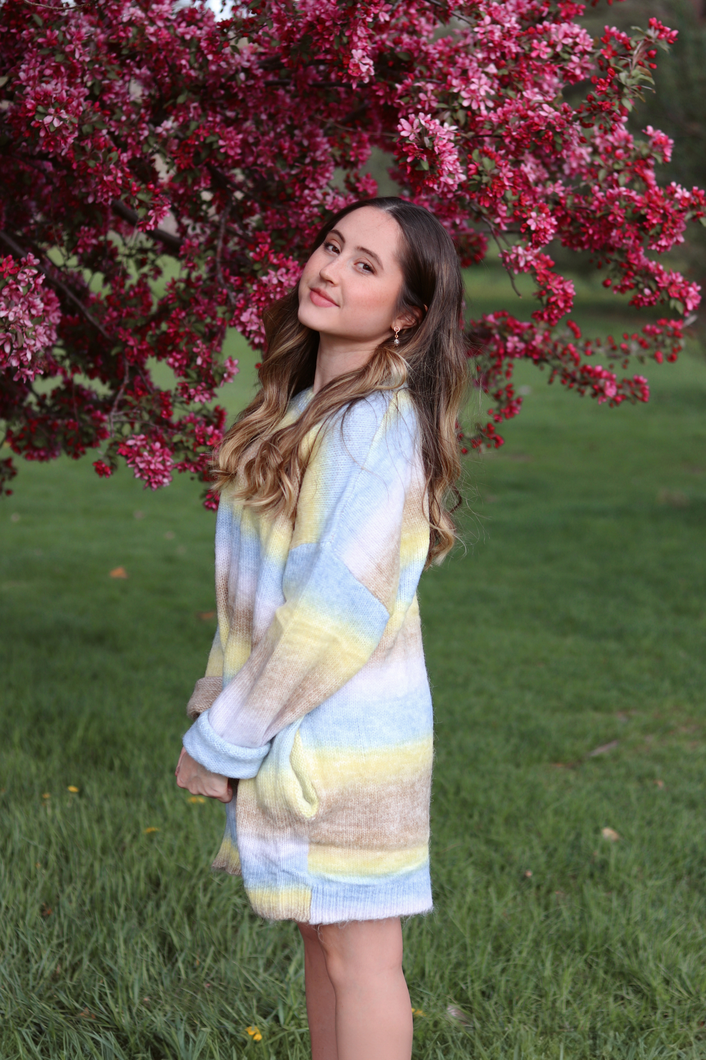 Woman in a colorful cardigan standing under a pink flowering tree