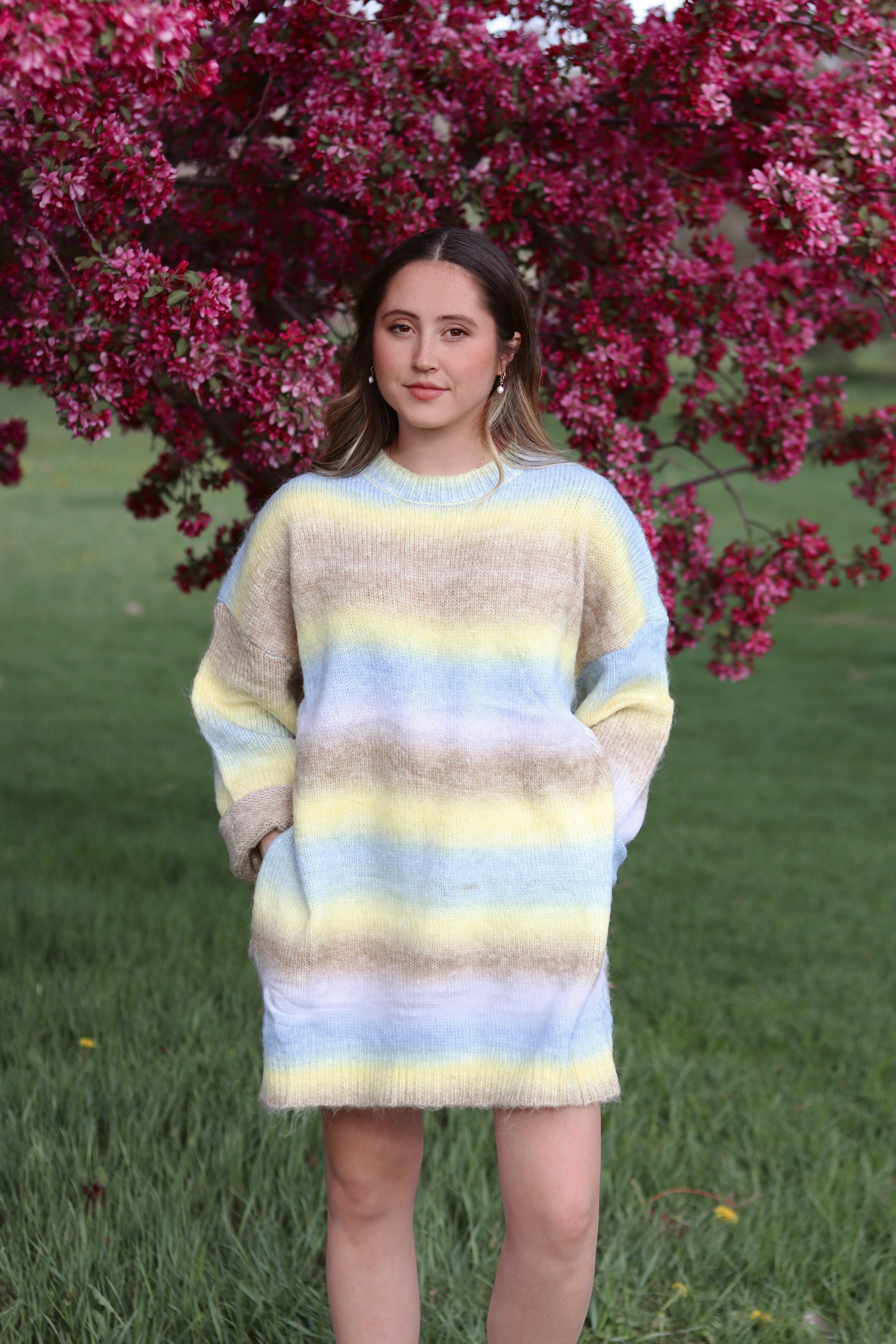 Woman wearing a colorful striped sweater dress standing in front of a flowering tree