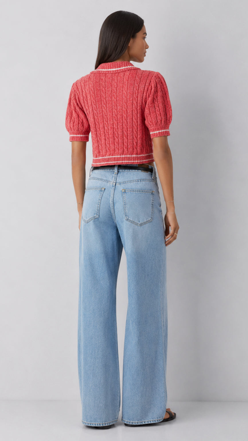 Person wearing a red knitted top and light blue jeans on a plain background