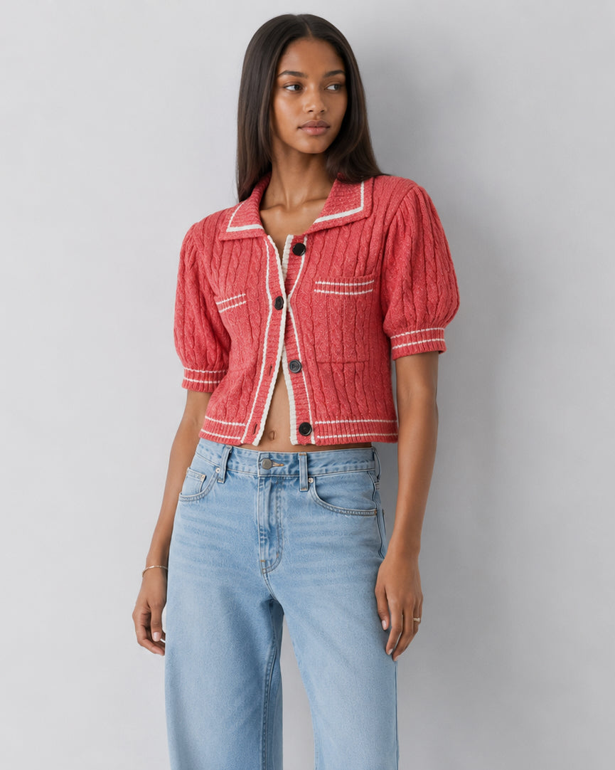 Woman wearing a red cropped jacket and light blue jeans against a gray background