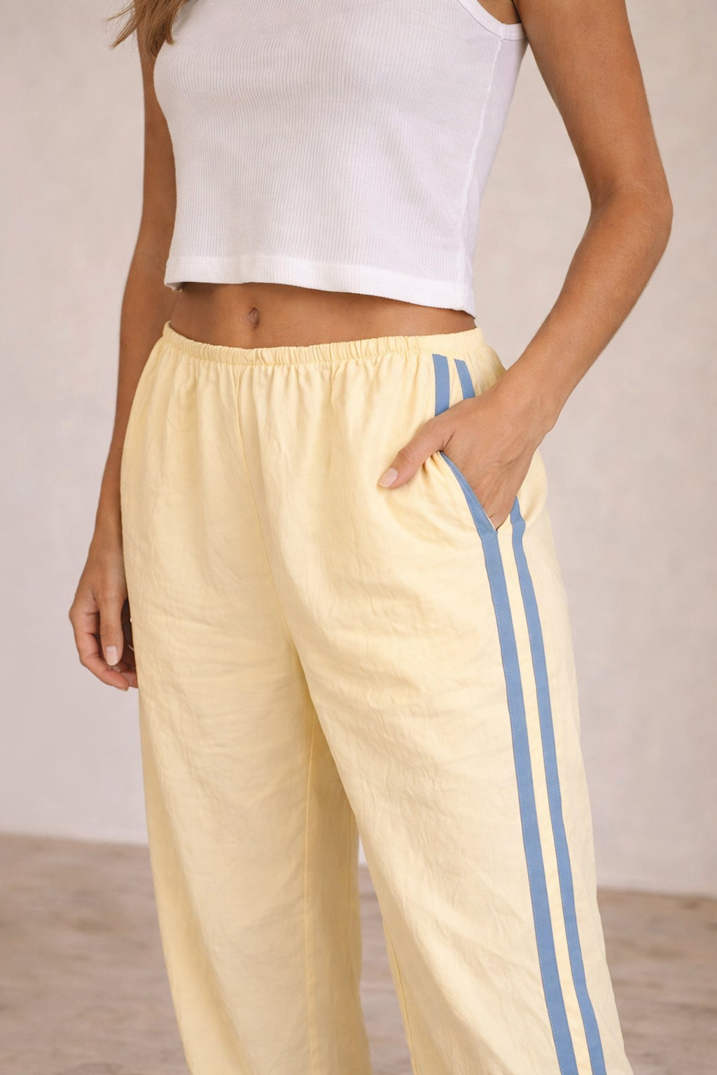 Person wearing light-colored pants with blue stripes and a white top against a neutral background