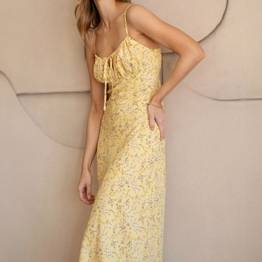 A woman wearing a yellow floral midi dress with a tie front detail and side zipper, with the dress reaching mid-calf.