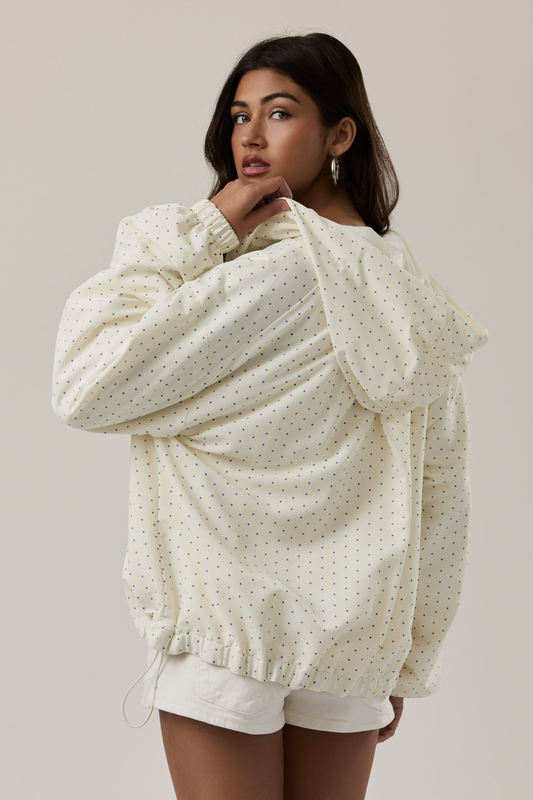 Woman wearing a cream-colored polka dot blouse with white shorts on a plain background